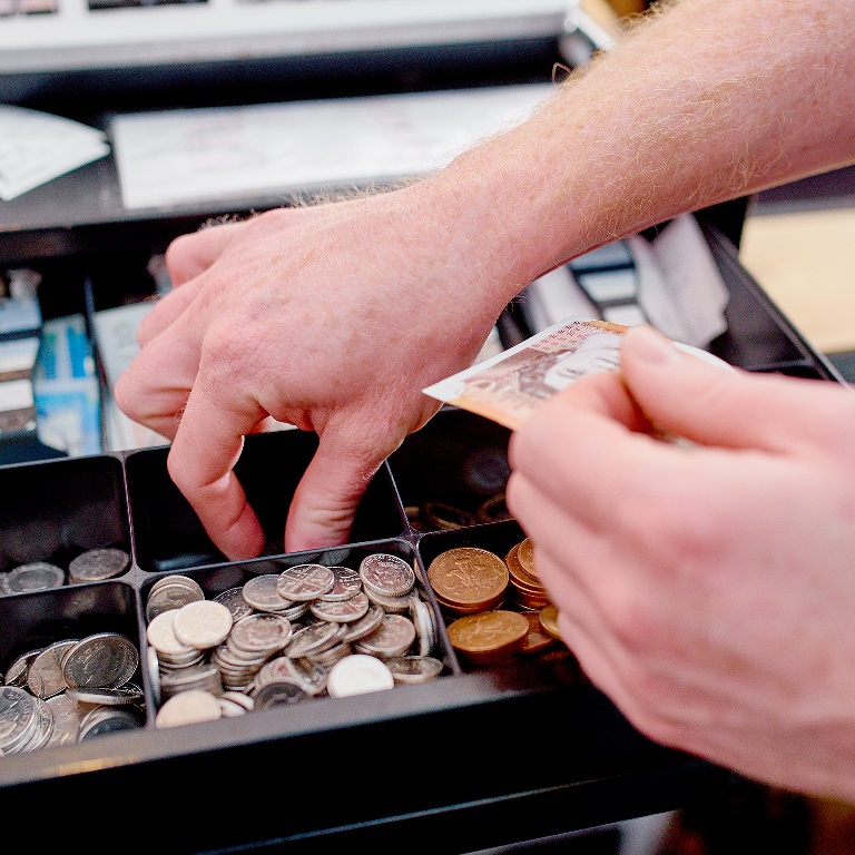 Employee handling cash in hospitality at a restaurant cash register, counting coins and holding a banknote during a payment transaction